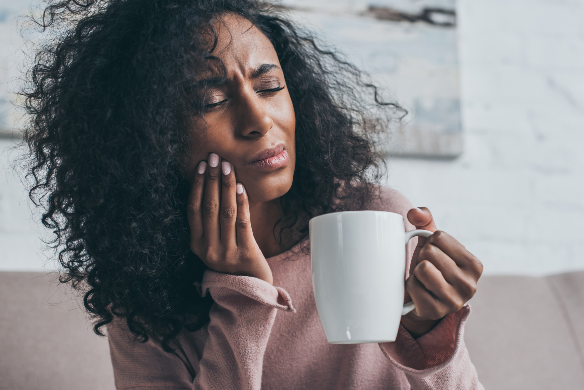 black woman experiencing TMJ pain holding coffee cup