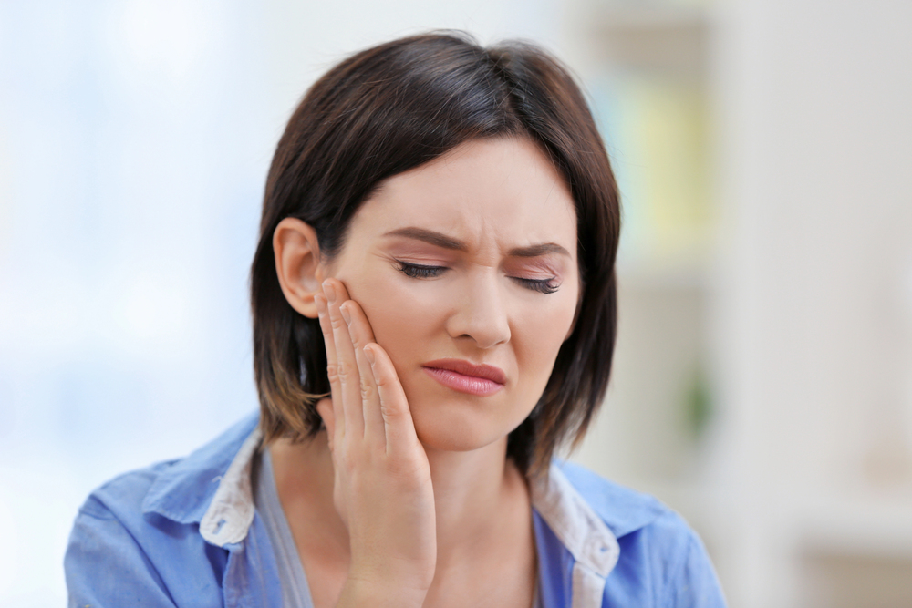 A woman wincing and holding a hand to her face due to dental pain that may require a root canal