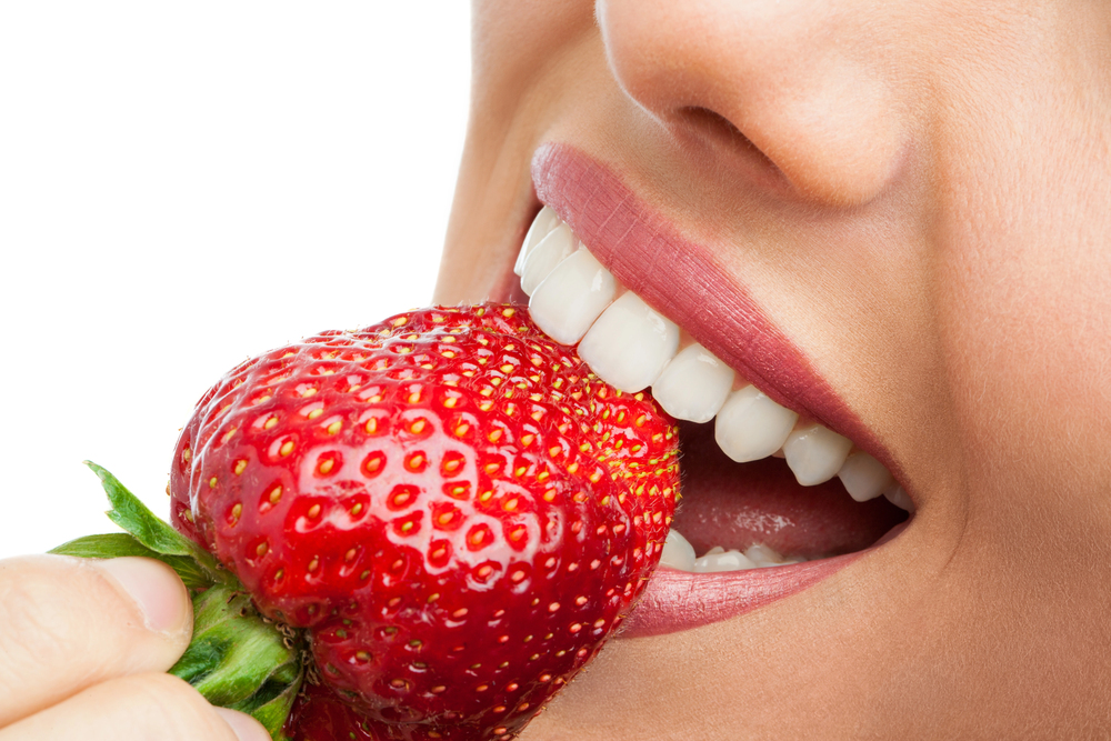 A closeup of a person biting into a berry, a food known to cause tooth discoloration