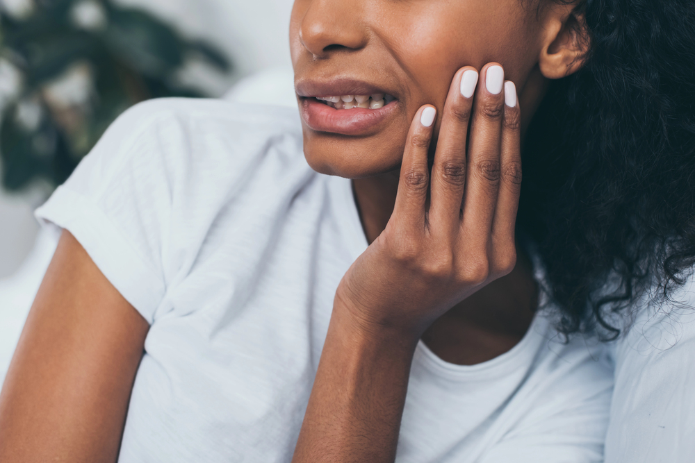 close up of black woman wincing and touching her jaw because of jaw pain