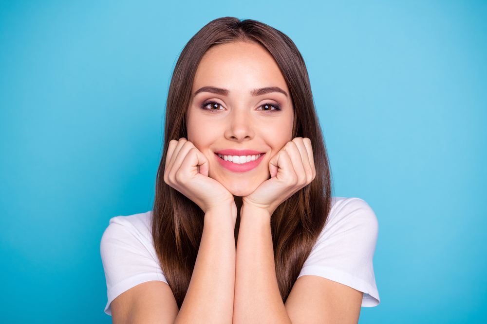 portrait of brown-haired woman resting her chin on her hands with blue background