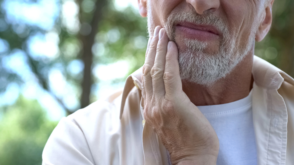 older man wincing and touching side of his face because of root canal infection