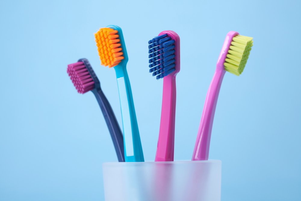 four colorful toothbrushes in a cup on blue background