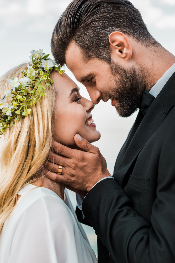 beautiful couple on their wedding day, man holding woman's face in his hands, looking in each other's eyes and smile