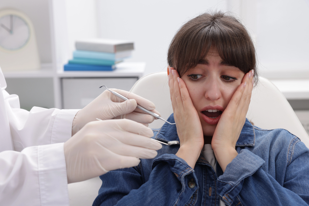 woman with fear of the dentist touching her face and scared looking at dentist hands holding instruments up to her mouth