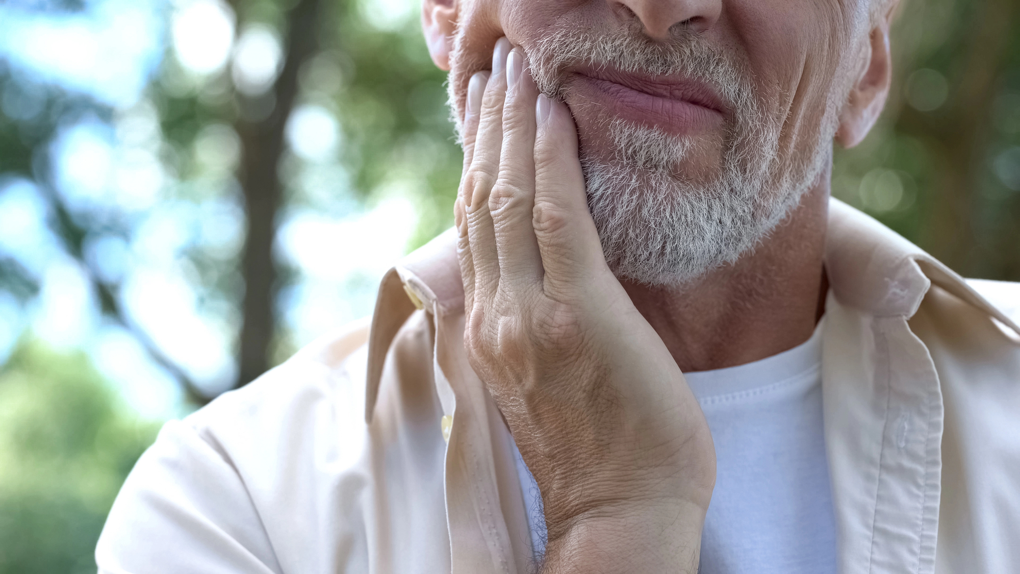 An older white man clutches his right jaw as if he has a stiff jaw.