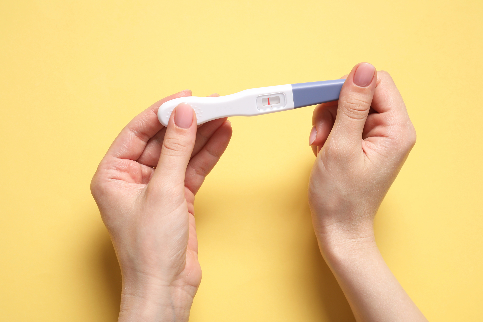 Hands hold a pregnancy test against a yellow background, illustrating how dental care with a dentist in Homewood, IL, can lead to easier conception and better pregnancies
