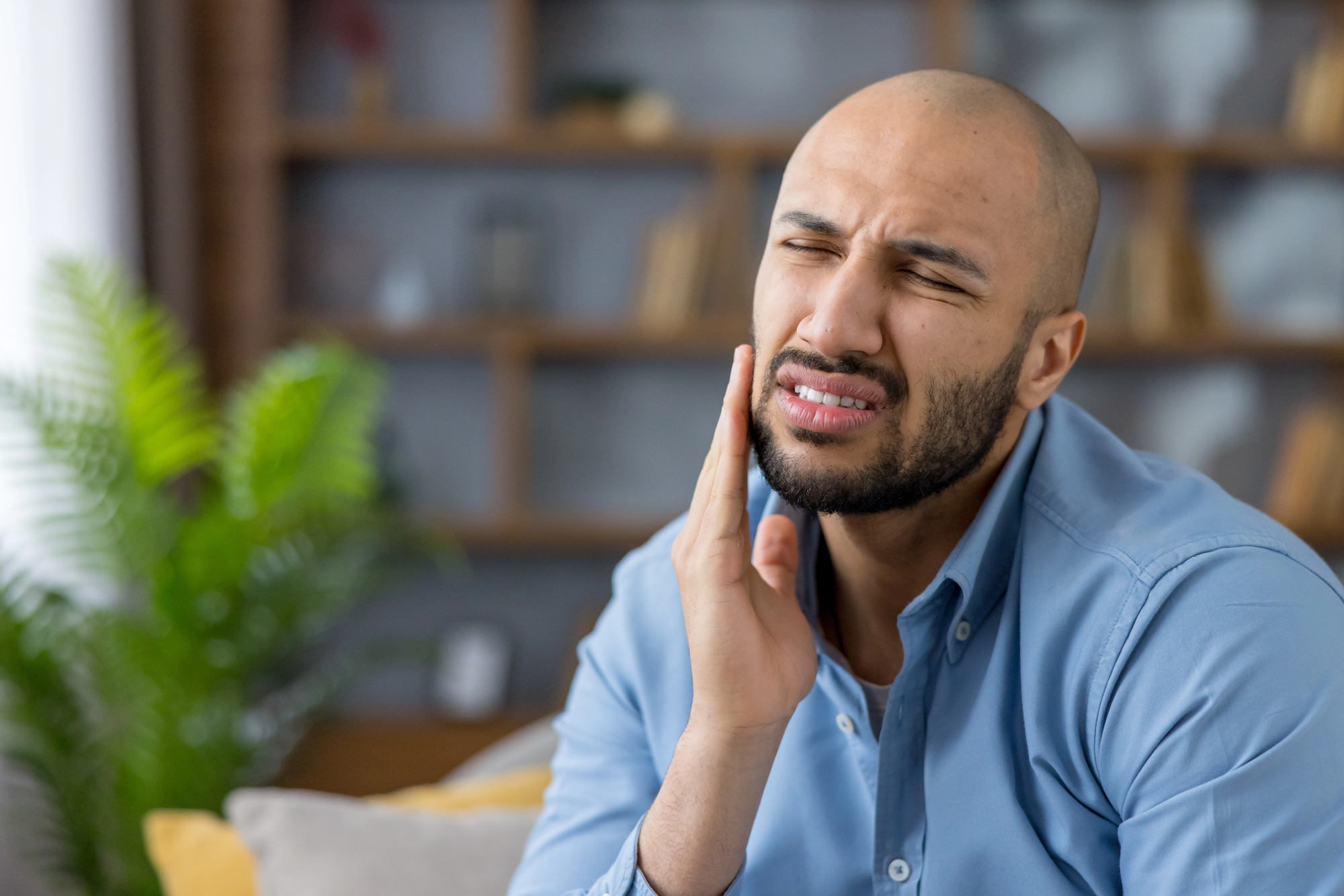 Picture of a light-skinned man of color holding his right cheekc and wincing in pain as he contemplates 