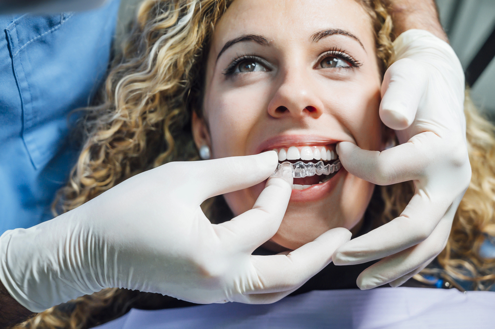 Patient with clear braces smiling as a dentist wearing gloves adjusts them in her mouth (close-up).