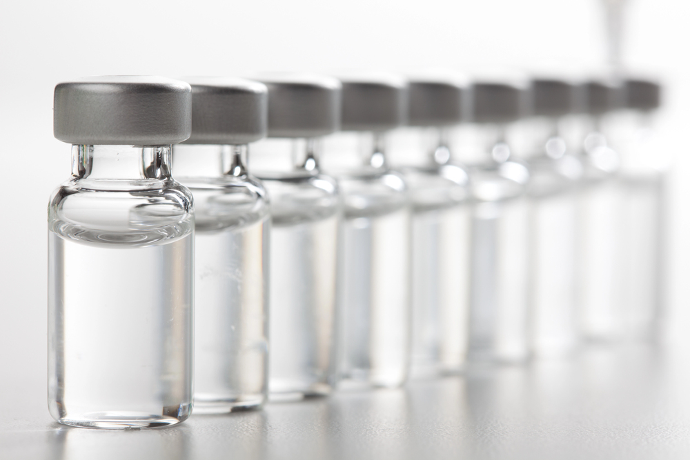 Row of small glass vials with gray caps containing clear liquid, lined up on a white surface in a lab setting.