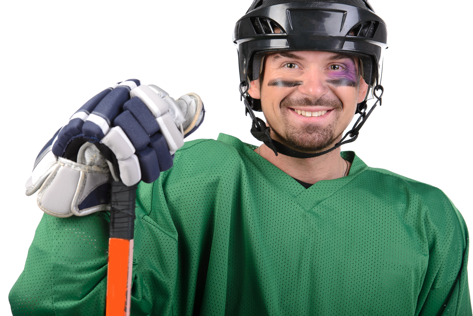 Hockey player in a green jersey and black helmet, smiling, gripping an orange hockey stick toward the camera.