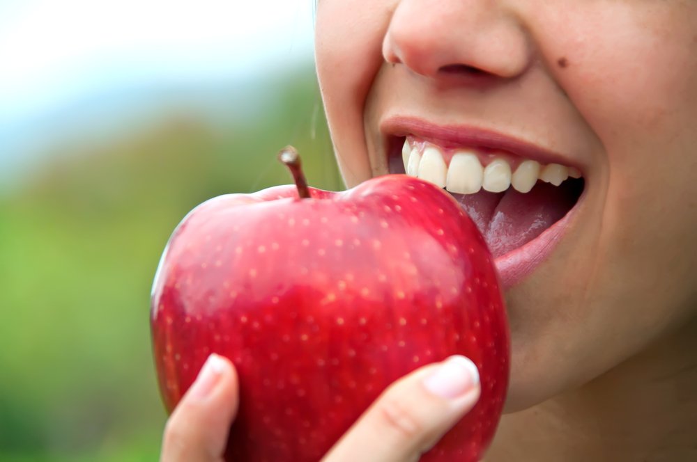 BitingAnApple Smiling woman enjoying an apple with long-lasting dental implants
