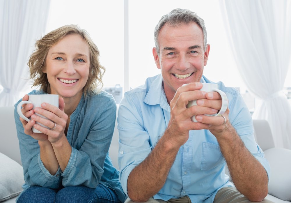 SmilingMiddleAgedCoupleSittingOnTheCouchHavingCoffee Man resting at home with soft food during All-on-4 recovery